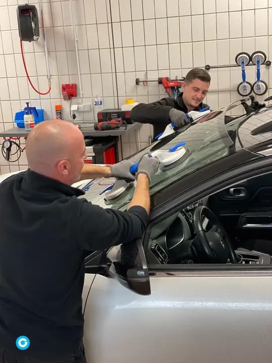 Deux techniciens posant un pare-brise neuf à l'aide de ventouses dans l'atelier
